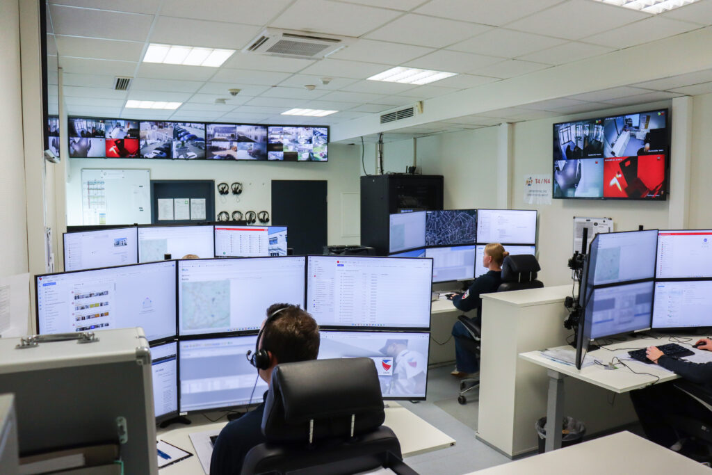 Zwei Sicherheitsmitarbeiter von Pond Security sitzen an Schreibtischen mit mehreren Monitoren, die Überwachungskameras zeigen, in einem Kontrollraum der NSL.