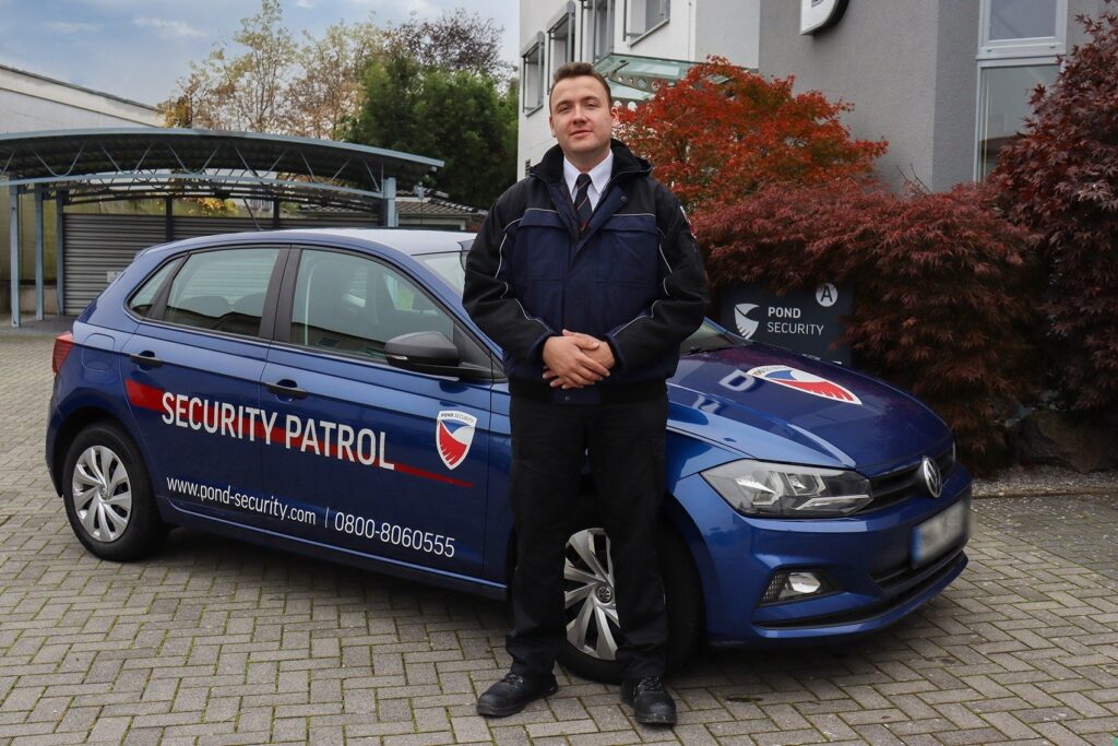 Interventionsdienst-Fahrer in Uniform steht vor blauem Pond Security Fahrzeug mit Aufschrift 'SECURITY PATROL' und Firmenlogo.
