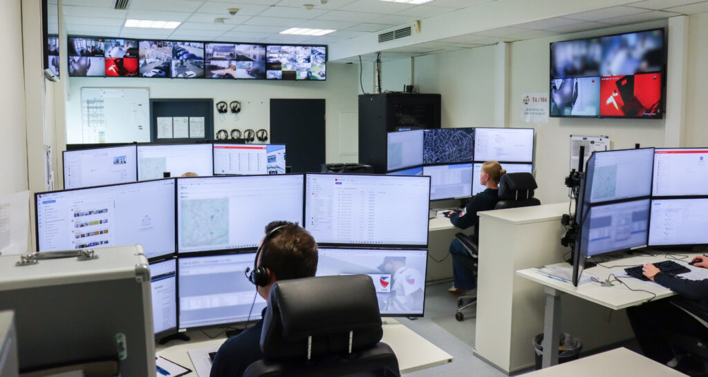 Zwei Sicherheitsmitarbeiter von Pond Security sitzen an Schreibtischen mit mehreren Monitoren, die Überwachungskameras zeigen, in einem Kontrollraum der NSL.